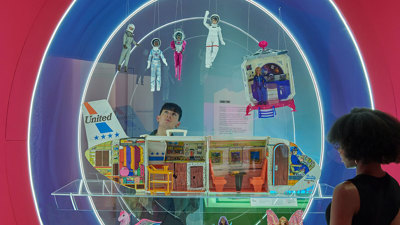 A circular display features a United Airplane cut in half to reveal places for barbie to sit and accessorise. Various barbies dress as astronauts and fairies are suspended around the plane on strings.