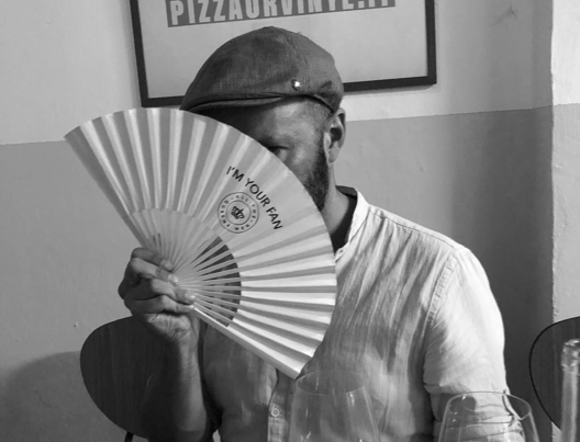 Mr Weir in a white linen shirt peeking from behind a fan that says ' I'm your fan'.