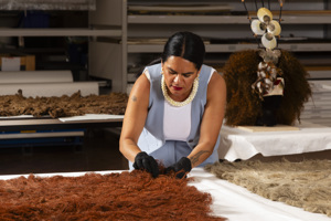 A woman wearing blue and white inspects a cloak in the museum collection store.