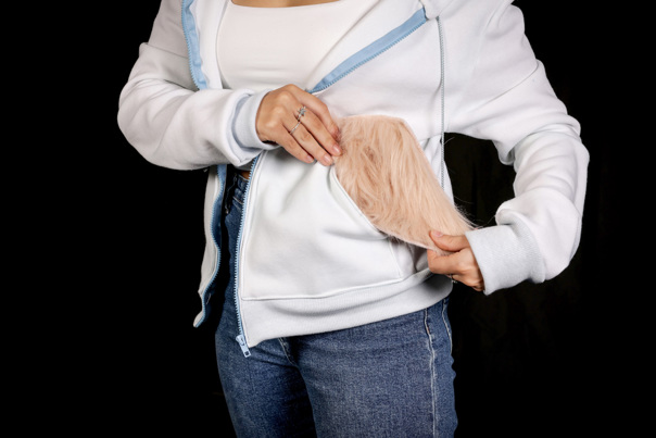 Person wearing a white hoodie and jeans. They hold a turned out pocket of the hoodie, which features a faux fur panel.