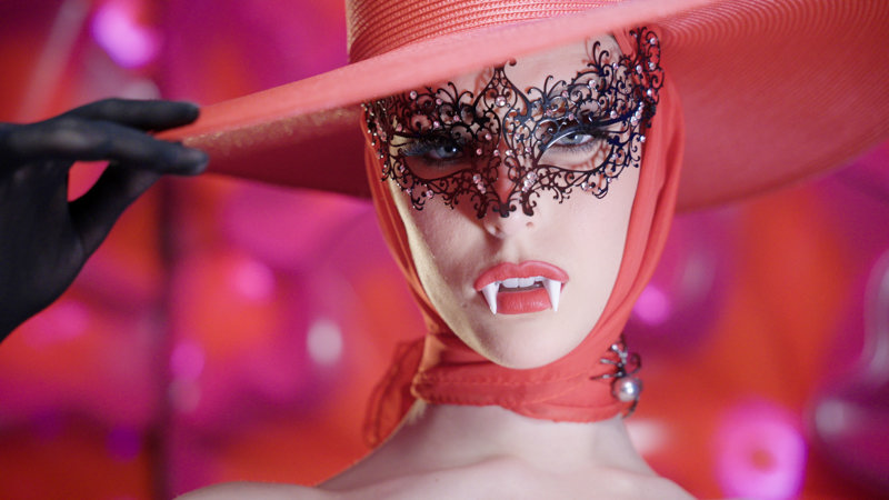 A woman wearing a wide-brim red hat and a black lacey mask.