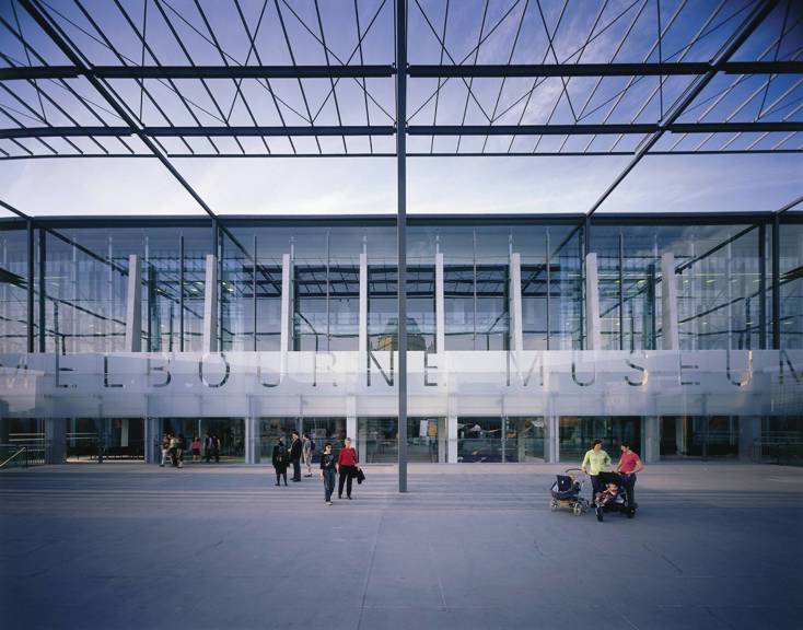 Exterior of Melbourne Museum showing glass facade and entrance, with people on the plaza