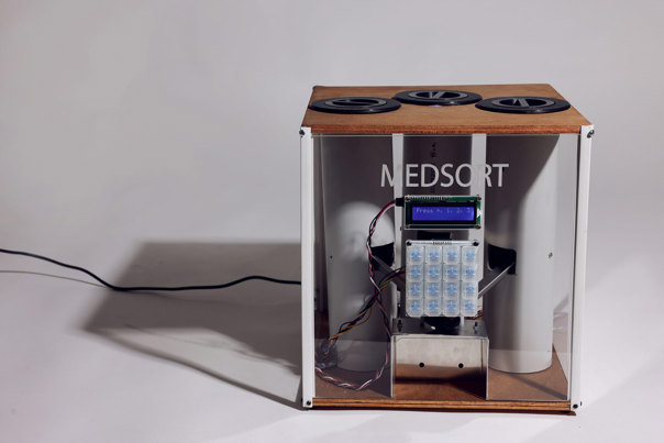 Transparent acrylic box with wooden top featuring three circular openings, revealing internal electronics including a digital display, LED array, and wiring components.