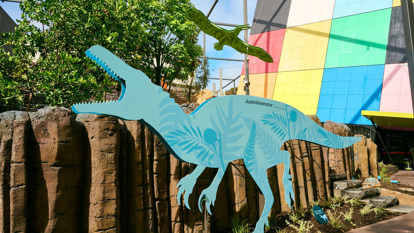 A blue silhouette of a Raptor-esque Australovenator dinosaur illustrated with plants standing in the Gandel Gondwana Gardens