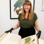 Woman smiling at the camera, holding a rare book open in front of her. She is wearing blue gloves