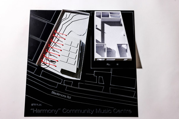 Grey architectural model on a black base, showing the building's exterior with a row of red accents, alongside an interior floor plan.