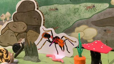 A ant and rock pile coloured illustration sits next to a plasticine mushrooms and carrots in a close-up of a bugs themed Diorama.