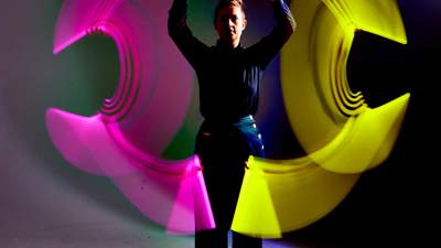 Person waving a light source in each hand to create a circle-shaped light pattern in a variety of colours.