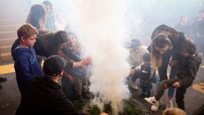 Children and parents gather around smoke during a smoking ceremony in the outdoor amphitheatre at Scienceworks.