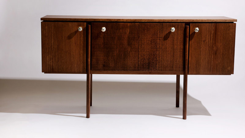 Low, rectangular sideboard in dark-stained timber with four polished-brass disc handles, three storage compartments with sliding doors, and slender squared legs.